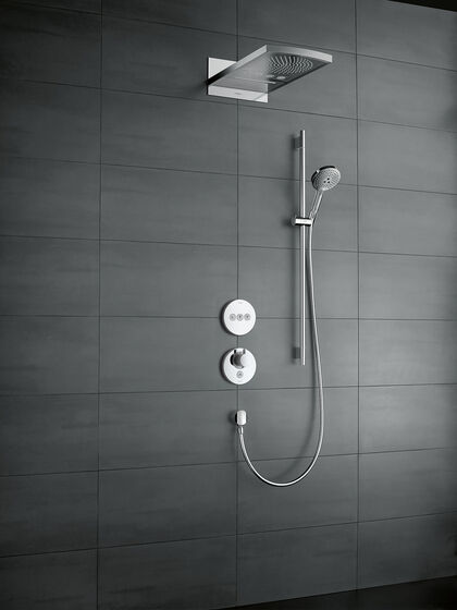 Grau geflieste Duschwand, an der ein rundes hansgrohe ShowerSelect Thermostat befestigt ist, sowie eine Duscharmatur mit Handbrause. Darüber befindet sich eine Kopfbrause.
