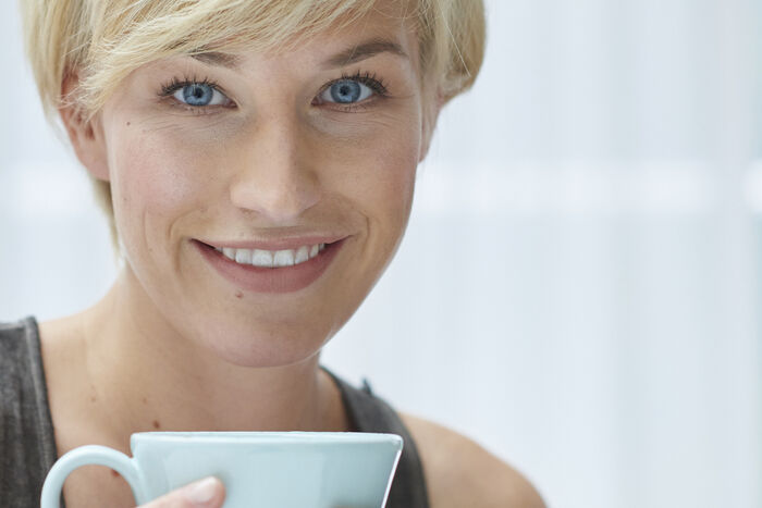 Hellblaue Teetasse wird von einr blonden Frau gehalten, die ein grauen Top trägt.
