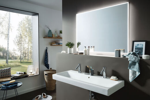 Ausschnitt aus einem modernen Bad, dessen Waschbecken mit einem großflächigen Lichtspiegel der Serie SmartLine 4.0 von Sprinz behängt wurde. Der Spiegel ist sanft hinterleuchtet.
