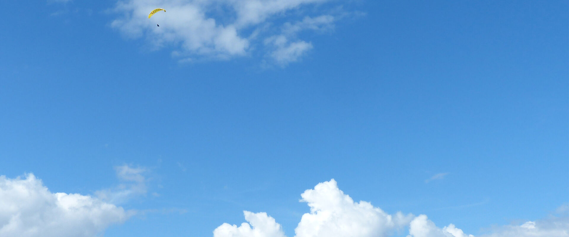 Blauer Himmel mit weißen Quellwolken und einem Paragleiter.
