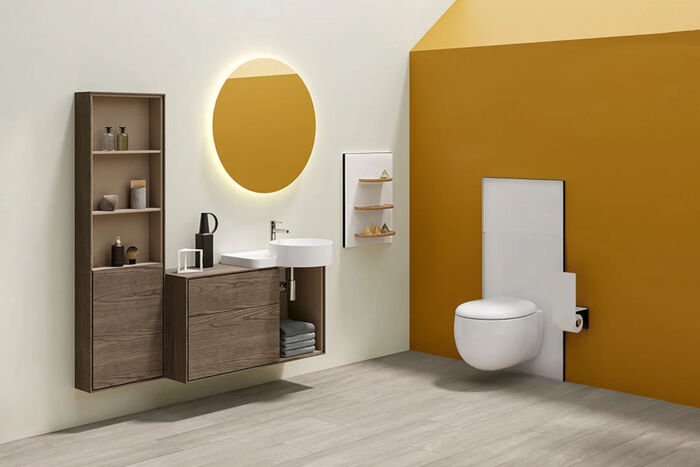Dunkle Möbel in Holzoptik aus dem Modulsystem VitrA Voyage mit integriertem Waschtisch auf der linken Seite und das passende WC mit weißer Spülkastenverkleidung vor einer gelben Wand auf der rechten Seite. 