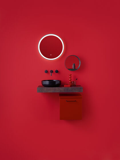 Waschplatz mit rotem wandmontiertem Badmöbelschrank mit schwarzen Griffen.