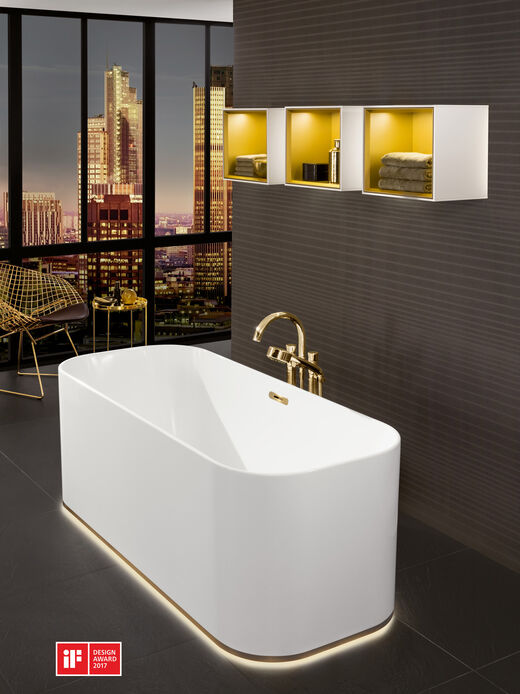 Freistehende Badewanne mit Lichtrand am Sockel. Goldene Standarmatur und beleuchtete Regale. Design Award.