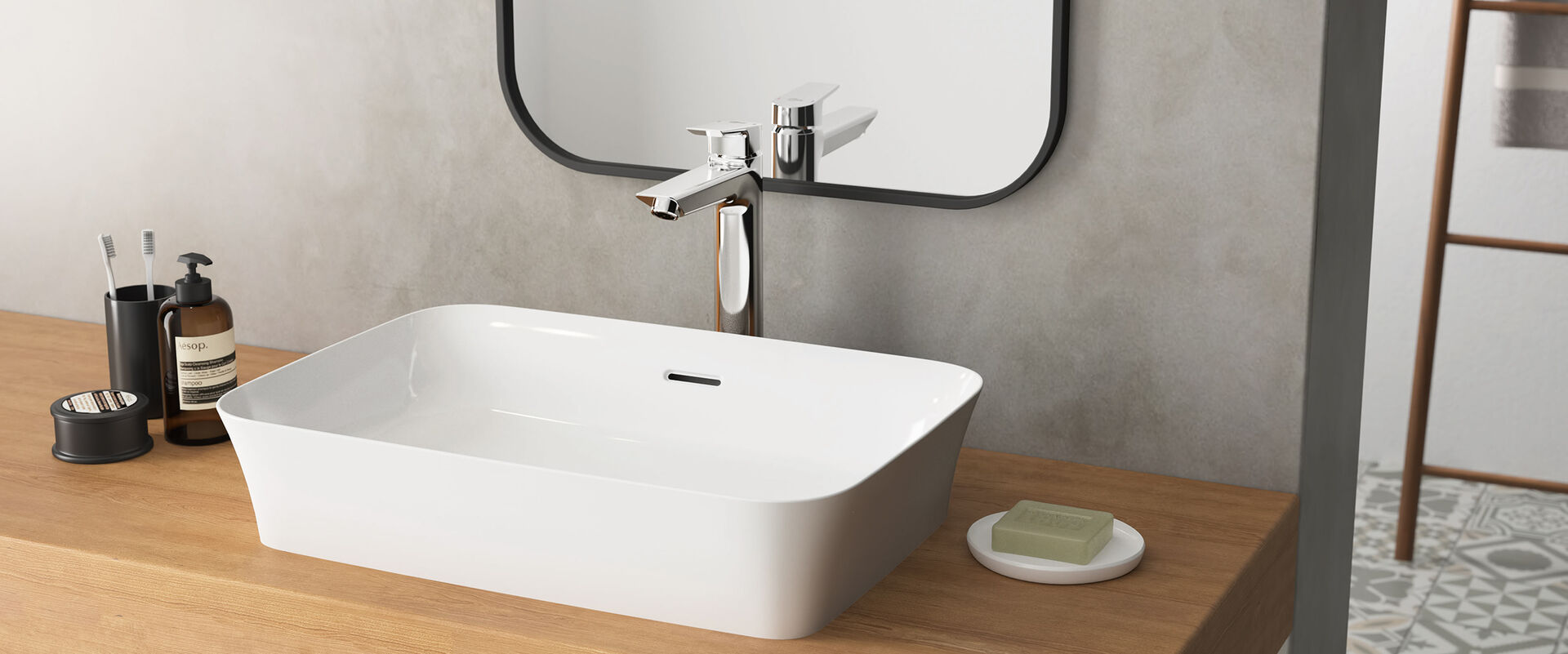 Waschbecken Ipalyss von Ideal Standard, dass auf einem hölzernen Waschtisch steht. Dahinter ist an einer grauen Wand ein Spiegel befestigt.