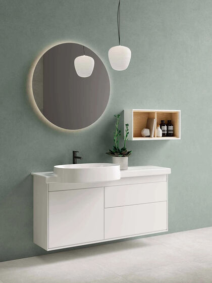 Waschtischunterschrank von VitrA Voyage mit dem dazu passenden Waschtisch in Weiß gehalten und kombiniert mit einem kleinen Wandelement, sowie einem großen, runden Spiegel.