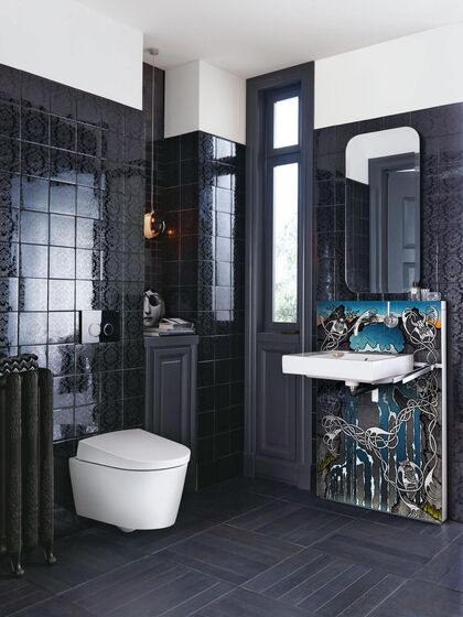 Künstlerisch individuell gestaltetes Altbau-Badezimmer von Geberit. Hohe Wände, schwarze Kacheln sind mit einem farbigen Kunstmotiv hinter dem Waschtisch und mit einem Dusch-WC der Serie AquaClean kombiniert.