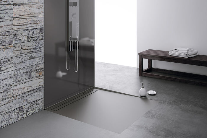 Graue Duschfläche mit Duschrinne und ein Glaslaminat als Duschwand mit Duschsystem.
