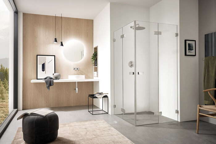 Helles Badezimmer mit Holz, Fenster und schönem Duschbereich. Die transparente Echtglasdusche Vega von Sprinz als Eckeinstieg komplettiert die Szene.