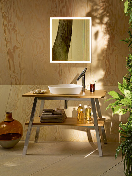 Waschplatz mit Holzablage und Stahlgestell. Rundes Aufsatzwaschbecken und Spiegel beleuchtet.