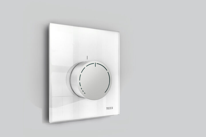 Runder Thermostatregler mit Glasabdeckung montiert an grauer Wand.