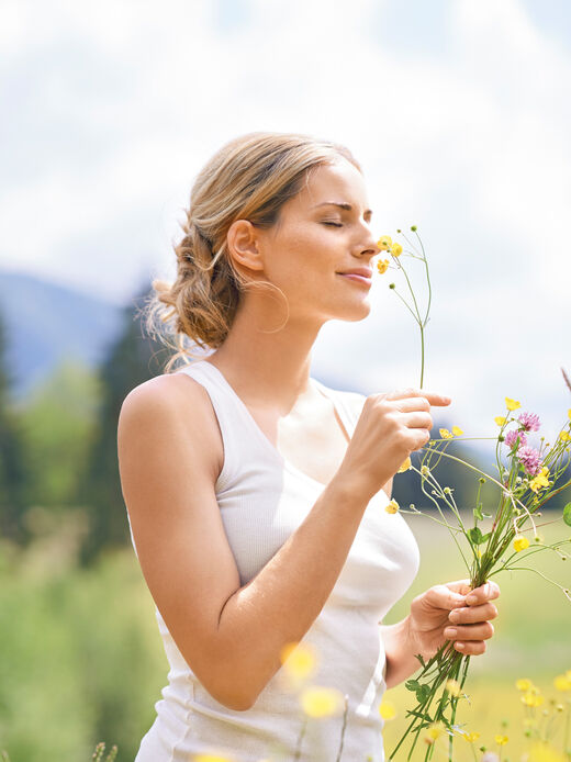 Frau in einer Blumenwiese hält gräser und Blumen in der Hand und riecht an ihnen.