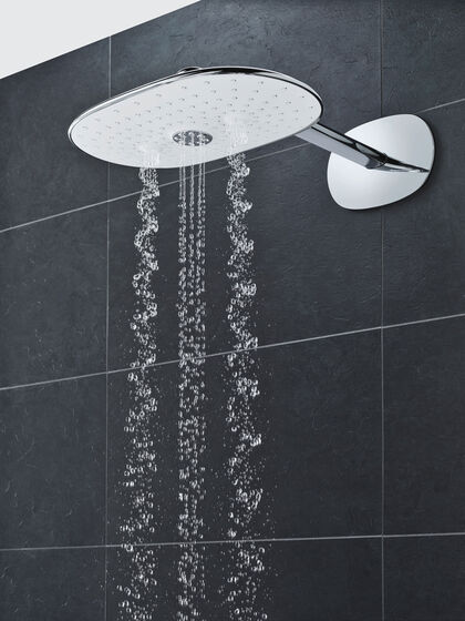GROHE Smart Control Duschkopf, der an einer schwarz-grau gefliesten Badezimmerwand befestigt wird. Aus der Kopfbrause fließt das Wasser in Teil gerader, teils spiralförmiger Form.