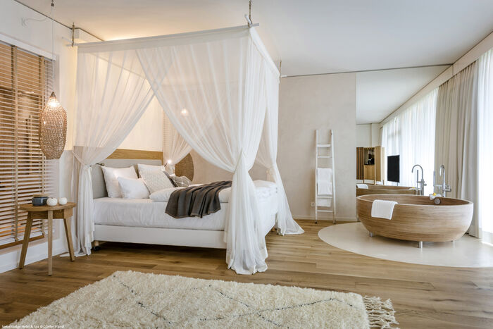 Große Suite in der Seezeitlodge mit Himmelbett in Weiß und einer freistehenden Holzbadewanne.