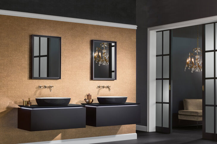 Badezimmer, an dessen Wand zwei Waschtische mit Artis Villeroy und Boch Waschbecken installiert sind. Darüber hängen Spiegel. Rechts befindet sich eine Nische, in der man einen Stuhl erkennt.