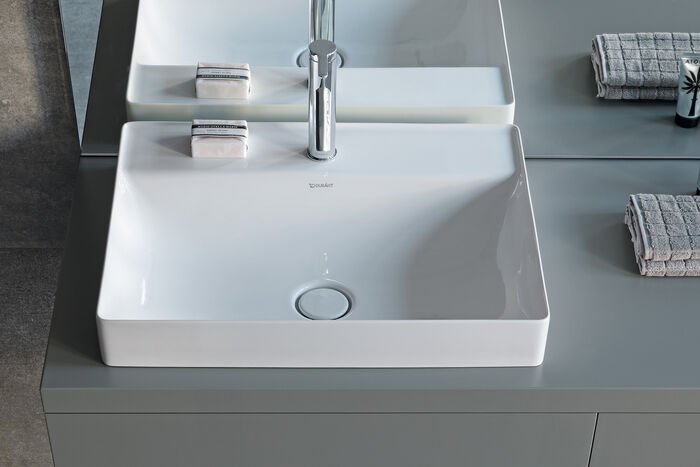 Blick auf ein weißes, eckiges Waschbecken mit schmalem Rand und mittigem Ablauf.