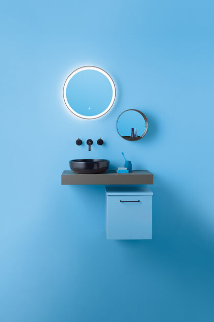 Blaue Waschtischkombi, bestehend aus Unterschrank, Waschtisch, der dann der Wand montiert ist, Aufsatzwaschbecken und Armaturen in schwarz sowie Spiegeln an der Wand.