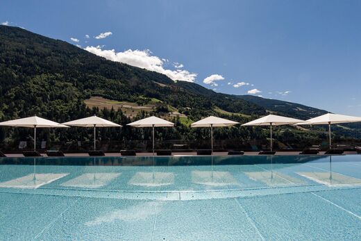 Pool Hotel Quellenhof Meran mit Liegen darum und Sonnenschirmen.