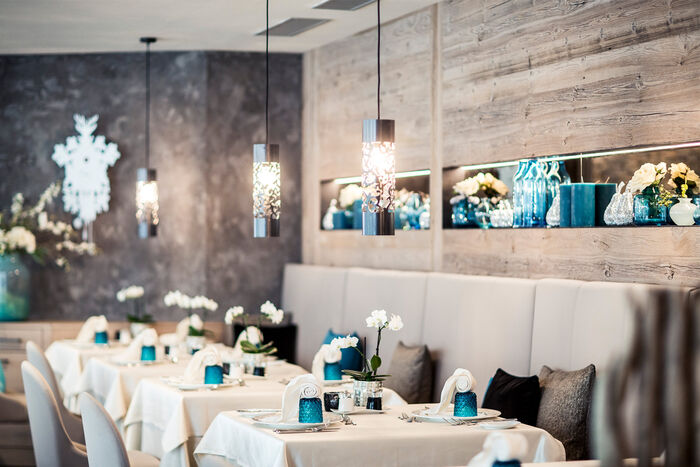 Restaurant im Quellenhof. Sitzbank und Stühle in beige. Eingedeckt mit Tischdecken und blauen Gläsern.