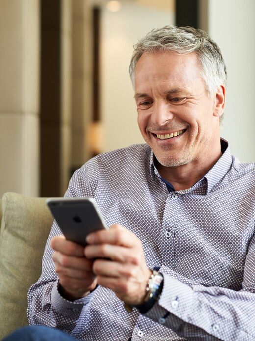 Mann um die 50 mit Handy in der Hand, auf dem erfreuliche Nachrichten abzulesen sind.