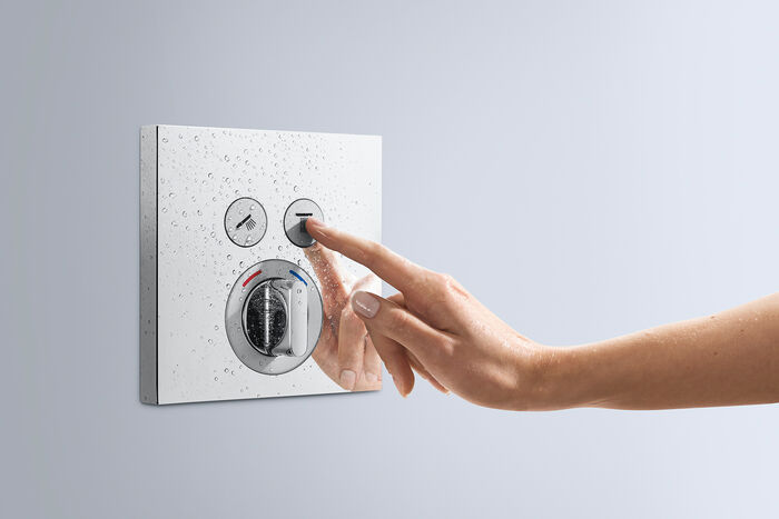 Shower Select Mixer von hansgrohe, in runder Form gehalten. Eine Hand betätigt den rechten Knopf des Thermostats.