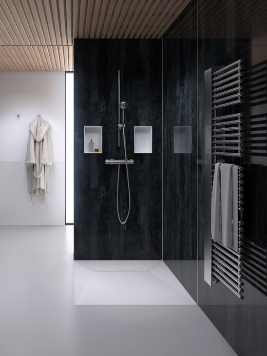 Dusche, in deren Duschwand als Ablageflächen zwei Duschboards Multistar Plan Plus von Schedel eingelassen sind. Rechts hängen Handtücher an einer Heizung, links hängt ein Bademantel im Hintergrund.