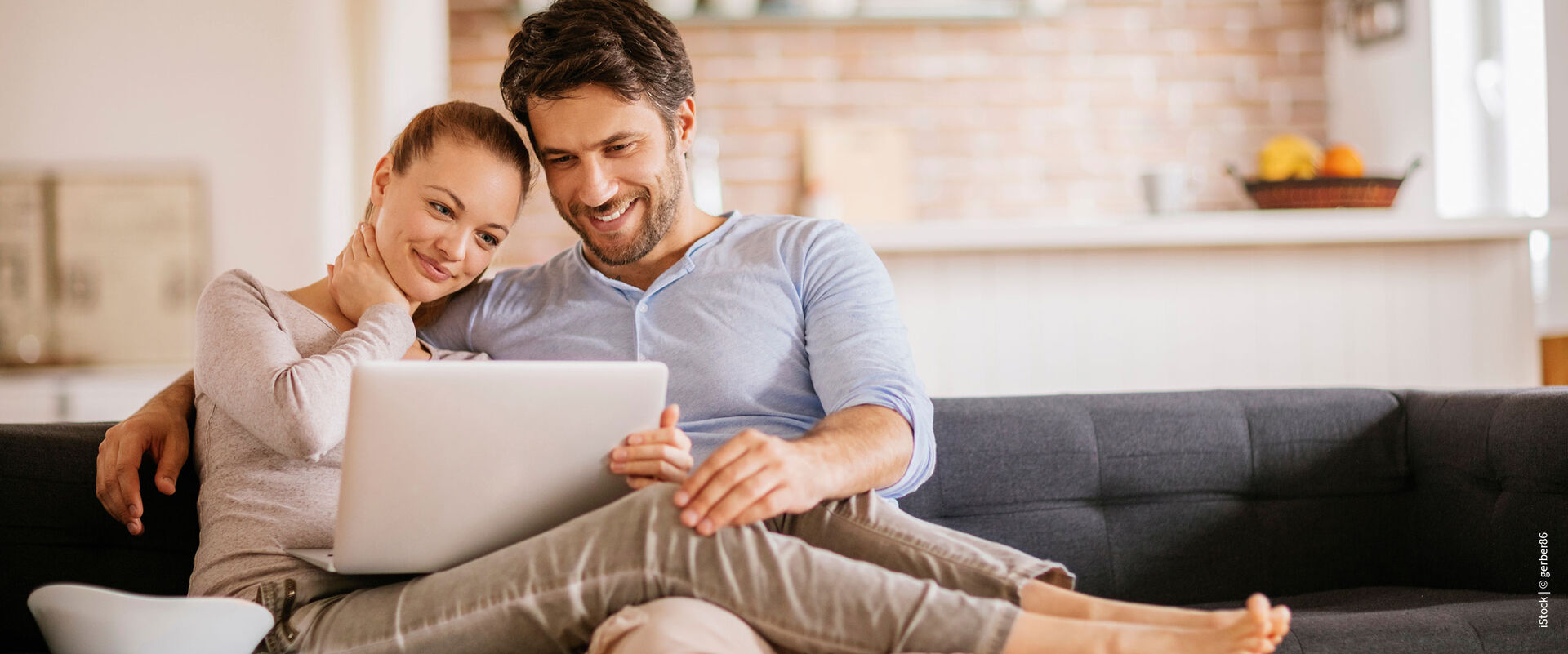 Junges Paar auf dem Sofa, das gemeinsam kuschelt und auf einen Laptop schaut – Syr Modelbild.