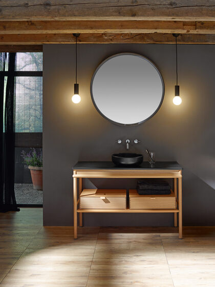 Waschbecken schwarz mit Badmöbeln aus Eiche und runder Spiegel. Mya von burgbad.