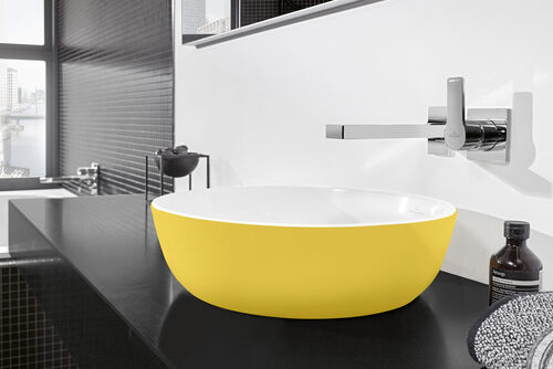 Gelbes Waschbecken Artis von Villeroy und Boch, das sich auf einem schwarzen Waschtisch befindet. Darüber hängt ein Spiegel. 
