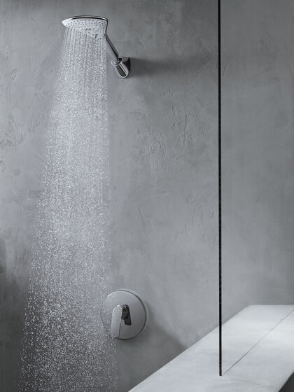 Wandmontierte Kopfbrause des Duschsystems Kludi Fizz, aus der Wasser strömt. Rechts befindet sich eine Duschglasscheibe.