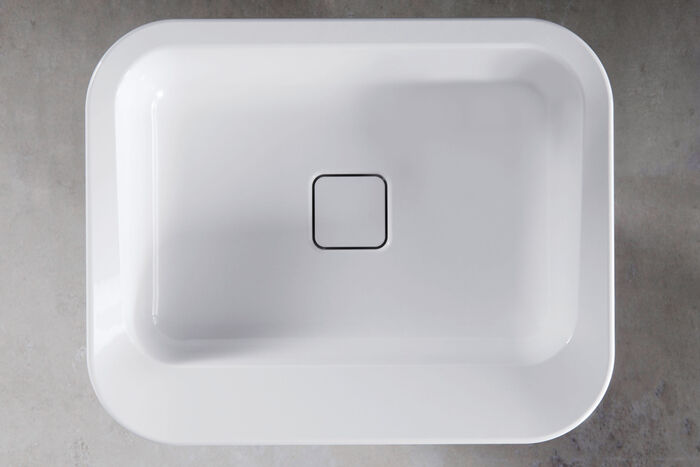 Weißes Waschbecken Emerson von Kaldewei, dass in einem Raum mit grauem Fußboden steht. Das Waschbecken hat eine eckige Form mit abgeflachten Ecken. Es wurde frontal von oben fotografiert.