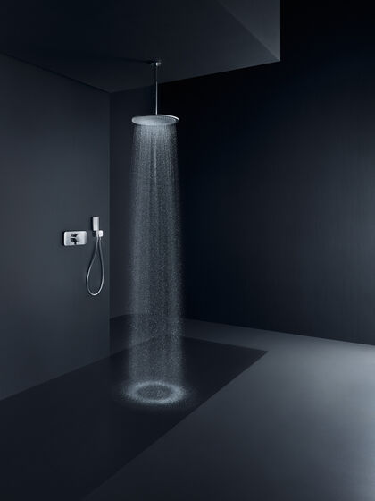 Eleganter, schwarzer Raum, in dem eine Axor Showers Deckenbrause installiert ist. Aus der Kopfbrause strömt Wasser, links sind Badarmaturen an der Wand befestigt.