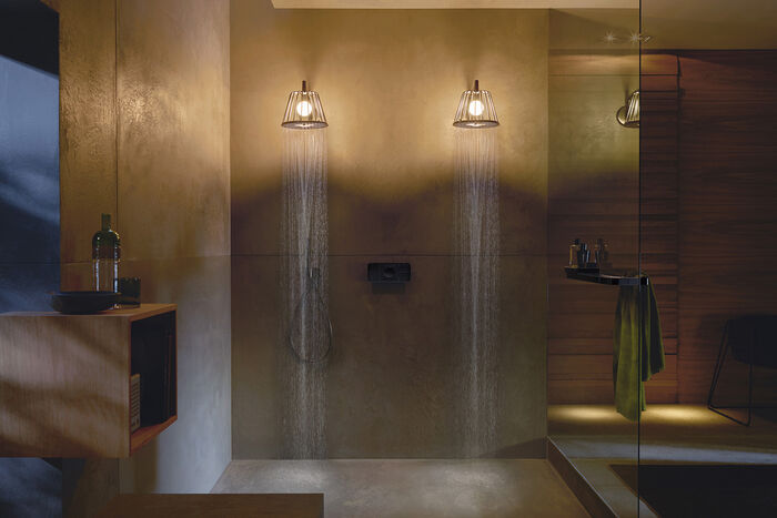 Badezimmer, in der nebeneinander zwei AXOR Nendo Kopfbrausen installiert sind. Die Kopfbrausen spenden Licht und tauchen den Raum in eine warme Stimmung ein.