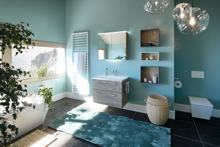 Helles Badezimmer mit Blauen Wänden. Bademöbel LUNA von Heibad. Neben dem Waschbecken mit Unterschrank und Spiegel befindet sich links eine Heizung, rechts mehre Regalelemente. Nebenan steht ein Wäschekorb, ganz links befindet sich die Toilette.