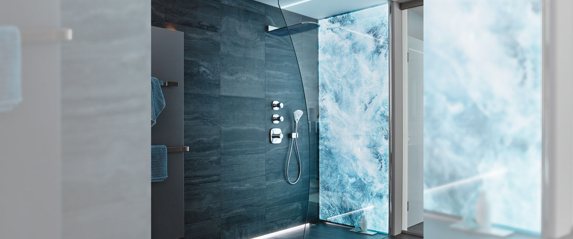 Duschkabine mit einer Spritz Premium LED Wandverkleidung, auf der sprudelndes Wasser abgebildet ist. Die restliche Dusche ist graublau gefliest.