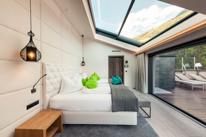 Weißes Doppelbett in Suite mit großem Deckenfenster und Terassentüre.