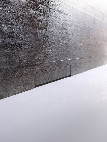 In einer Dusche mit grau gefliester Wand ist ein Geberit Wandablauf installiert. Der Ablauf scheint fast unsichtbar hinter den Fliesen versteckt zu sein.