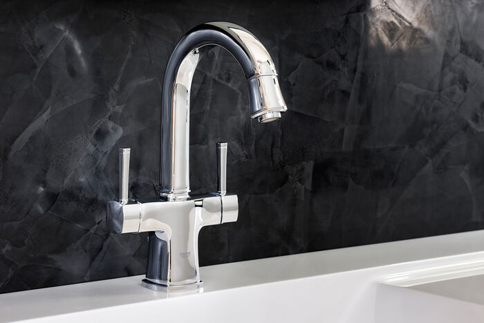 GROHE Grandera™ Wasserhahn Einhebelmischer chromfarben rund vor schwarzer Wand.