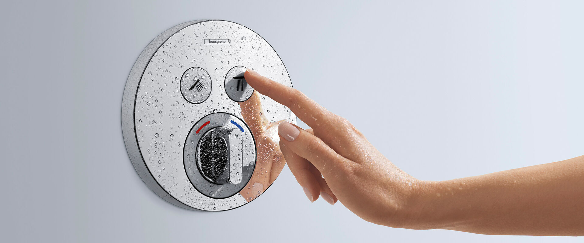 Shower Select Mixer von hansgrohe, in runder Form gehalten. Eine Hand betätigt den rechten Knopf des Thermostats.