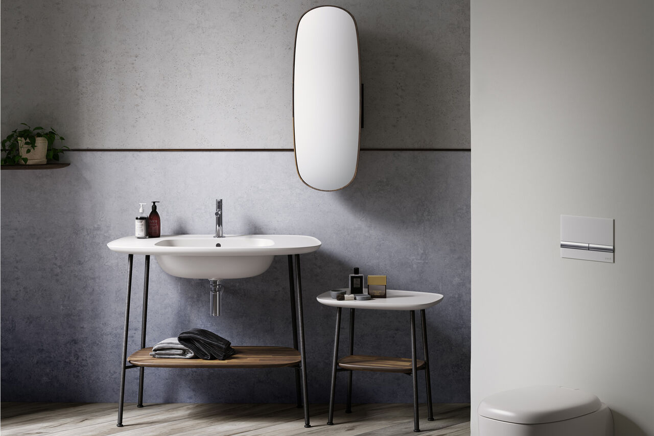 Badmöbel Plural von VitrA Vintage Waschplatz: Kombination von Waschbecken ohne Unterbau – sondern auf filigranen Füßen der VitrA Badmöbelserie Plural – und Beistelltisch mit Spiegel. Organische Formen, betonfarbenes Ambiente.