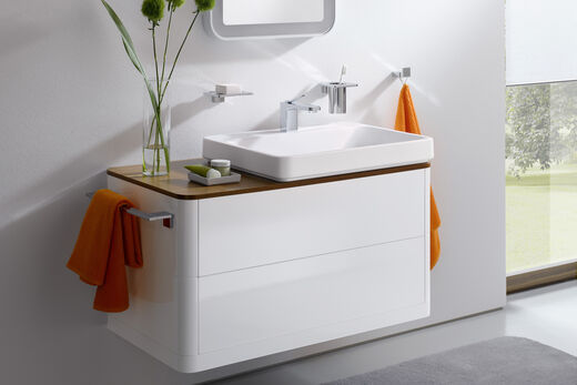 Weißes Badmöbel mit eckigem Aufsatzwaschbecken und seitlichem Handtuchhalter in Chrom.