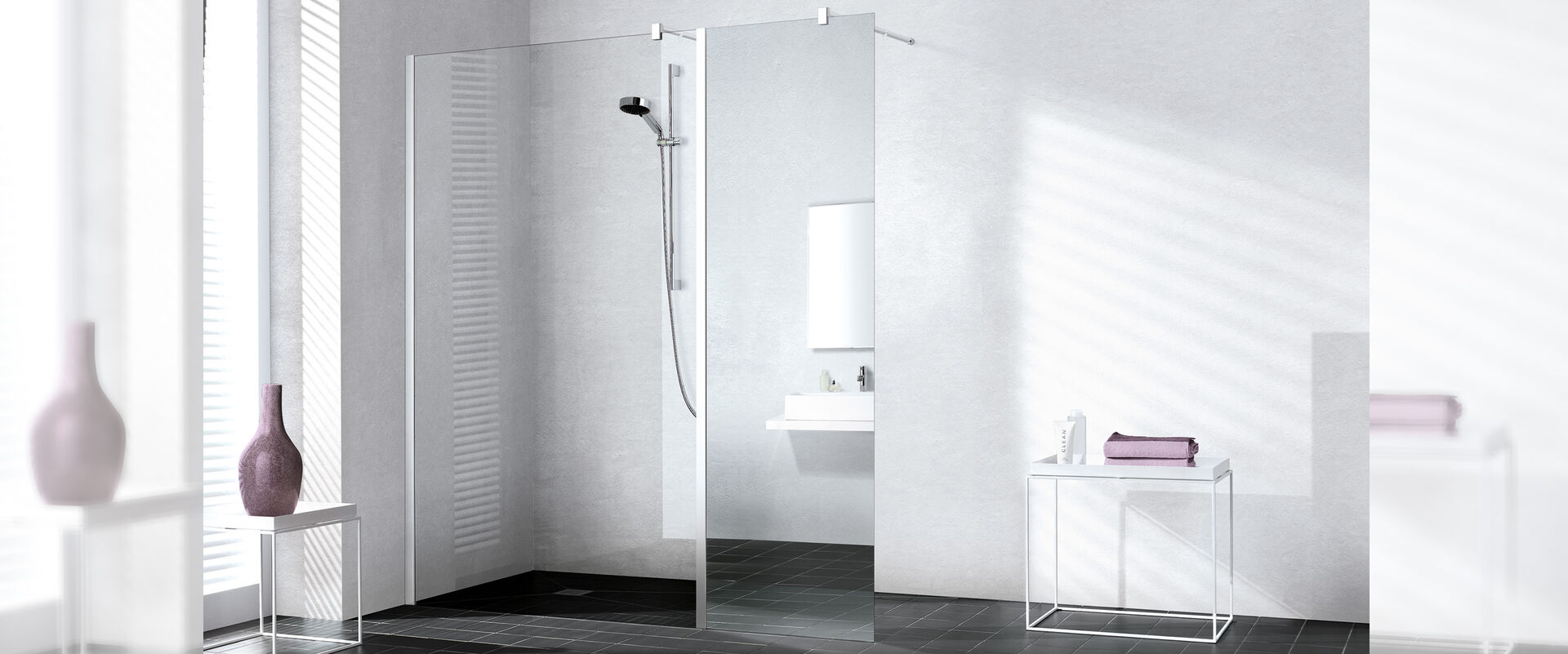 Kermi Walk-In XB Bodenebene Dusche, an der eine Kermi Walk In XB Wall installiert ist. Die Dusche befindet sich in einem hellen Badezimmer, links stehen Designobjekte, rechts steht ein Tisch, auf dem Handtücher und Hygieneartikel liegen.