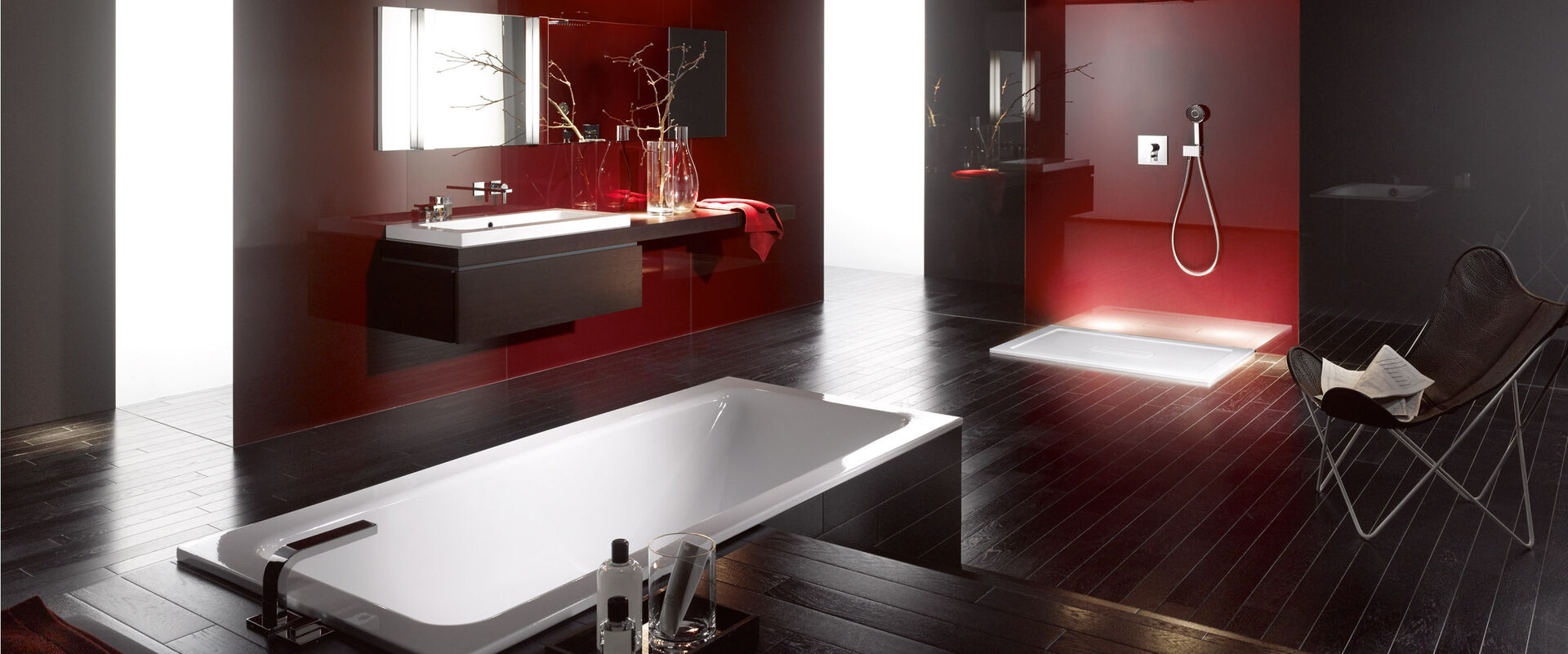 Badezimmermilieu mit Einbaubadewanne, Waschbecken und Dusche. Rote Wand Abendstimmung. Produkte BETTEOne von Bette.
