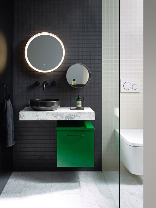 Grüner Badmöbelschrank unter Konsole weiss mit schwarzer Waschschale und runder Spiegel.