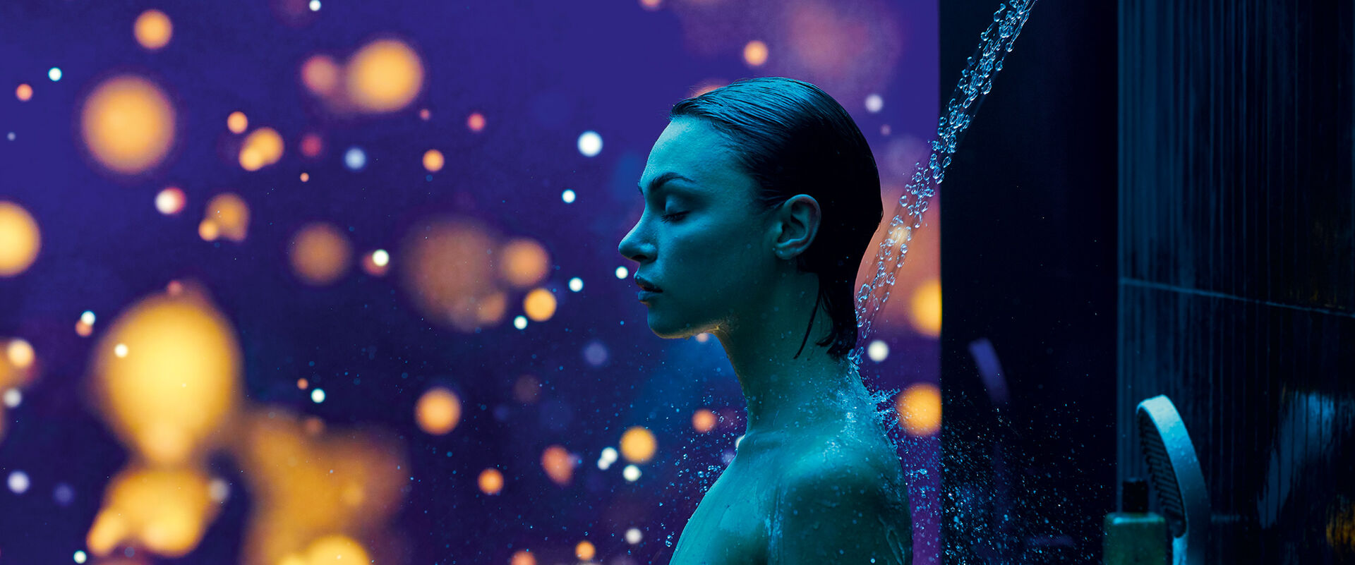 Oberkörper einer Frau inmitten eines mit RainTunes ausgestatteten Duschbereichs. Im Hintergrund leuchtet ein farbiges Bild mit großen, runden Lichtelementen.