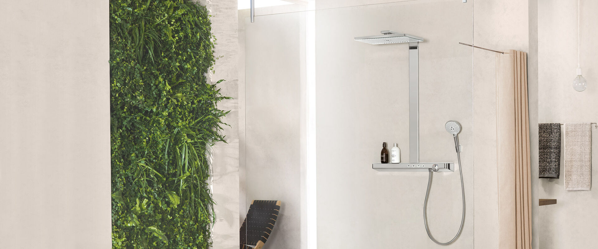 Helles Badezimmer, in dessen Dusche eine hansgrohe rainmaker select Kopfbrause installiert ist. Im Hintergrund hängen Handtücher. Links an der Wand wachsen grüne Pflanzen.