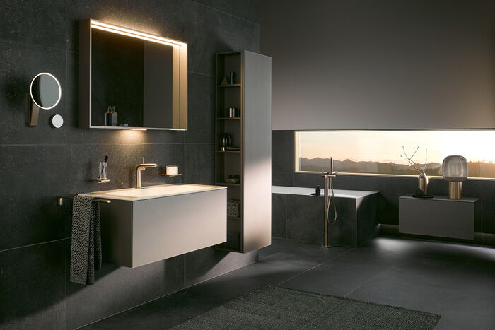 In grau gehaltenes Badezimmer KEUCO X-Line mit Waschbecken, Unterschrank und Spiegel. IN Hintergrund befindet sich an schmales, längliches Fenster mit Blick auf eine Berglandschaft.