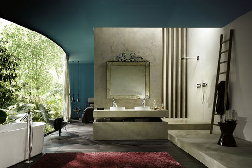 AXOR Starck Organic Sicht in ein Badezimmer mit Stand Badewannenarmatur und freistehender Badewanne. Blick auf Waschplatz mit zwei Waschbecken, Spiegel und Badarmaturen.
