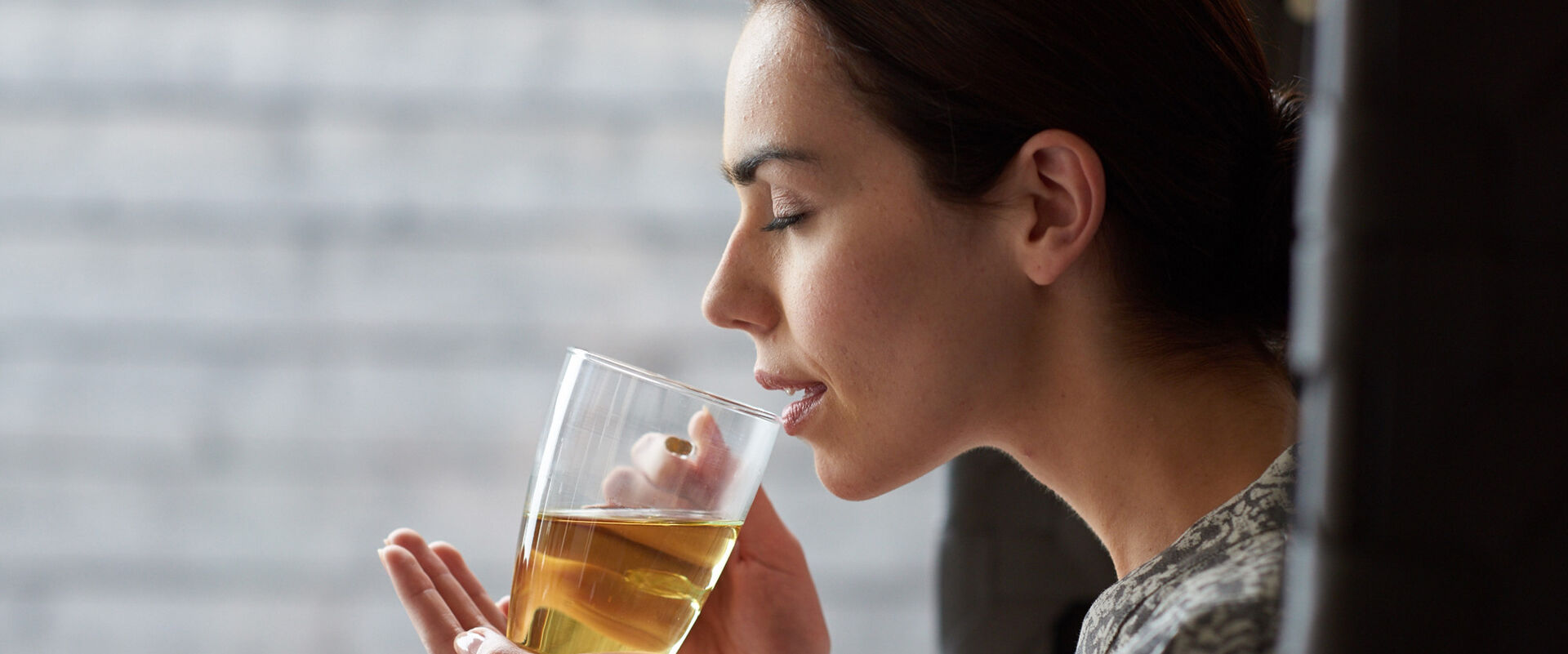 Dunkelhaarige Frau, die seitlich zu sehen ist trinkt Tee aus einem Teeglas.