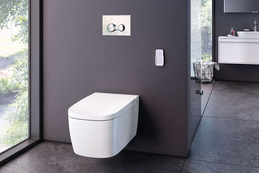 VitrA V-care Ausschnitt auf den WC-Bereich in einem Komfort-Badezimmer von VitrA. Dunkle Fließen und große Fenster sorgen für ein modernes Ambiente. Neben dem Dusch-WC V-care ist die Fernbedienung an der Wand angebracht.