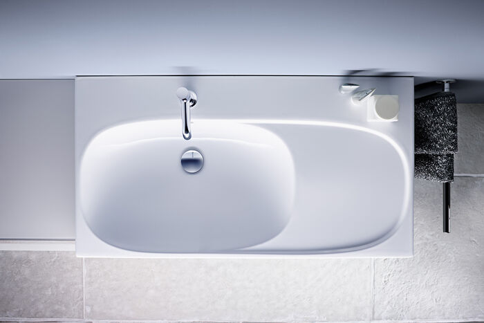 Weisses Waschbecken mit ovaler Schale und Ablage für Seife und Bad-Accessoires.
